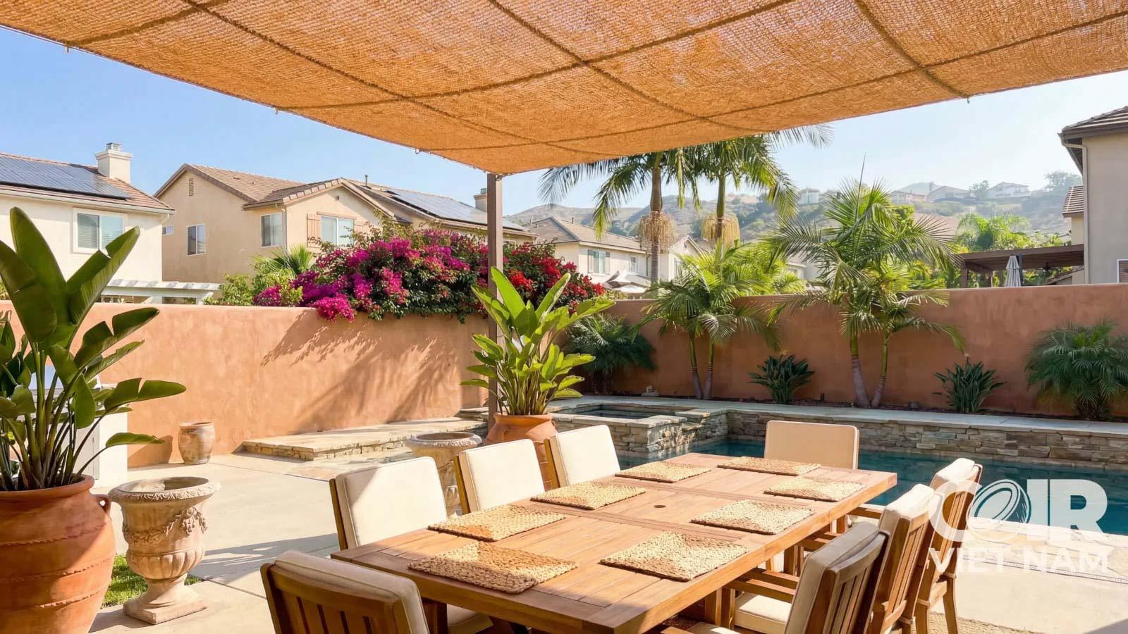 Coir shade sail installed above an outdoor dining area near a backyard pool, creating natural sun protection in a tropical residential garden.