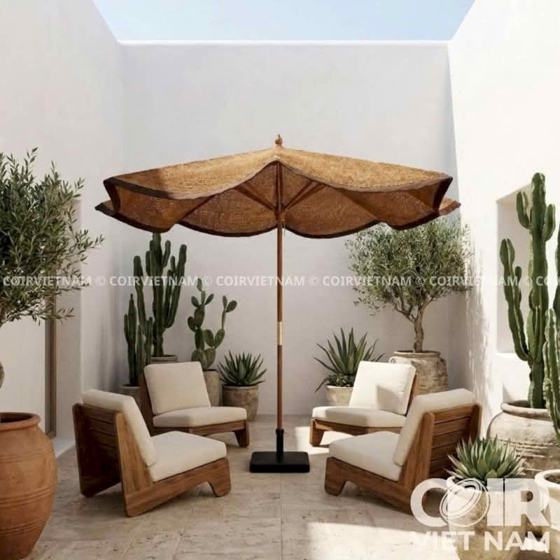 A large natural-fiber patio umbrella with a black base stands between two wooden lounge chairs with cream cushions in a sunlit outdoor patio setting with potted plants.
